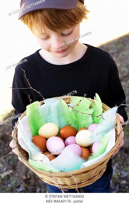 A boy holding a basket with painted eggs