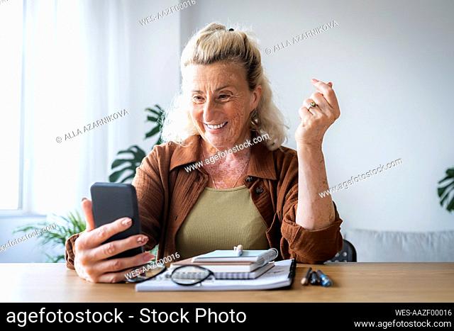 Happy senior businesswoman holding mobile phone at desk in home office
