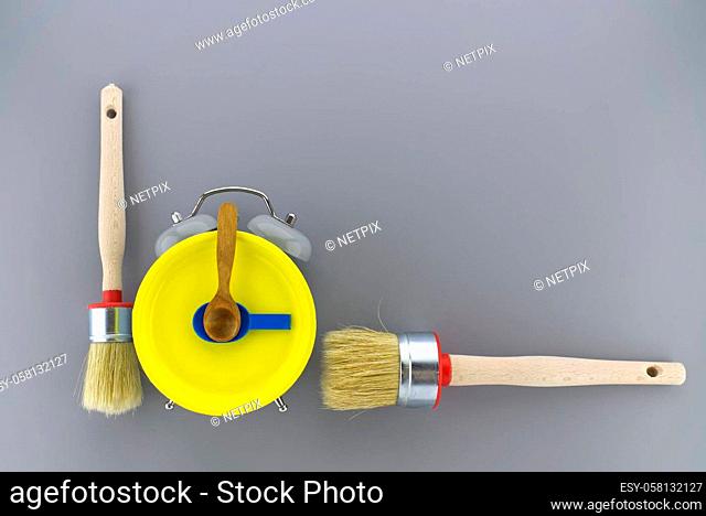 Creative DIY, decorating or renovations background with two clean bristle brushes and a colorful yellow alarm clock with tools for hands forming a border on...