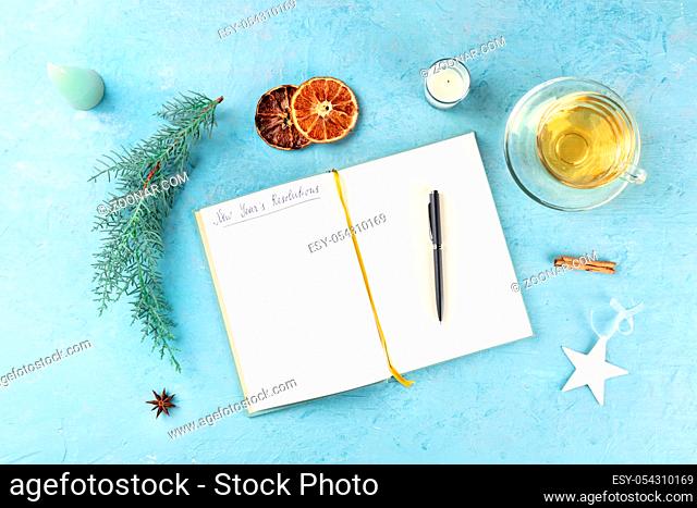 New Year's resolutions, flat lay overhead shot with the handwritten header and a place for text, on a blue background with Christmas decorations and hot tea