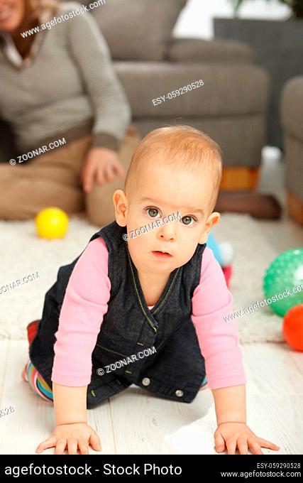 Portrait of cute baby girl kneeling on living room floor looking aside