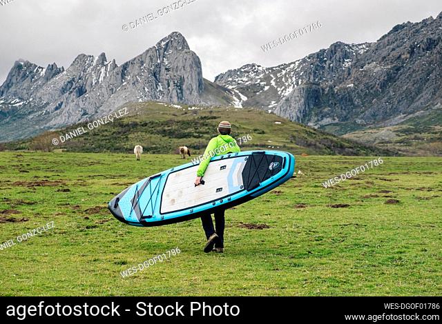 Mature man carrying paddleboard while walking on landscape, Leon, Spain