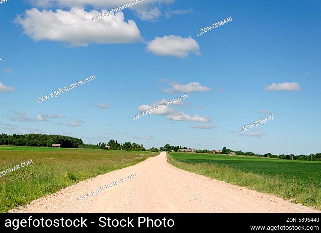 gravel country road continues into distance along the green fields on blue sky background