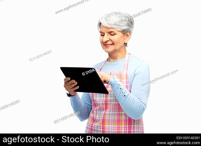 smiling senior woman in apron with tablet computer