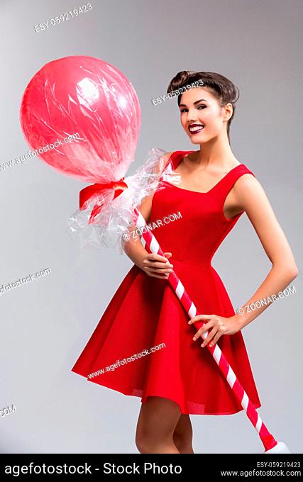 Beautiful young woman in red dress with huge lollipop candy. Surprised expression. Over grey background. Copy space
