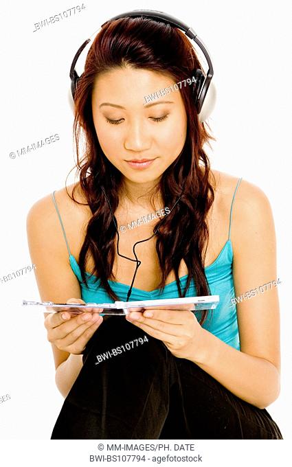 A pretty young asian woman looks at the CD case of the music she is listening to