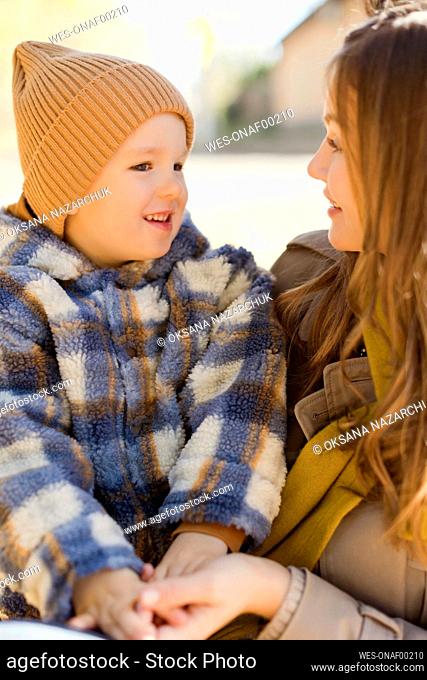 Cute boy wearing knit hat sitting on mother in park