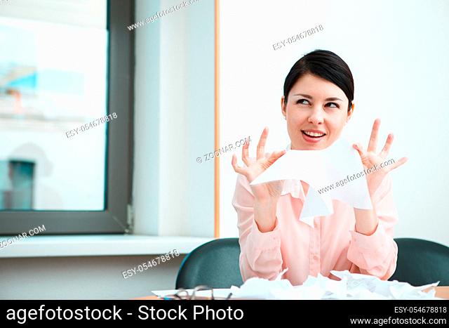business woman sitting her desk getting rid of old papers with pleasure