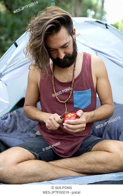 Man sitting in front of a tent peeling an apple