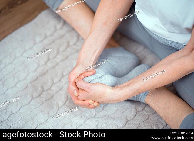 Hands Of A Mature Woman Touching The Toes Of Crossed Legs. Yoga Stretching. Selective Shot. Closeup