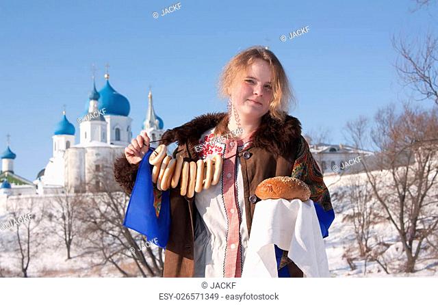 girl in russian traditional clothes with round cracknel against Russian landscape