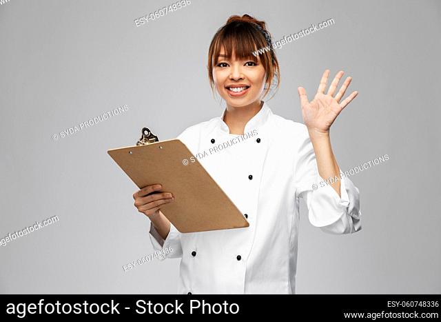 smiling female chef with clipboard waving hand