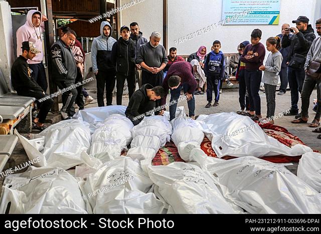 12 December 2023, Palestinian Territories, Rafah: Palestinian men kneel next to a relative body, killed following Israeli bombardment, at al-Najjar hospital