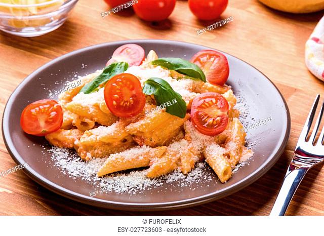 penne with tomato basil and cheese in brown plate on wooden table