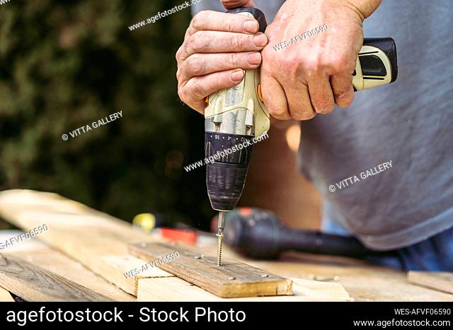 Senior man driving screw in wooden board