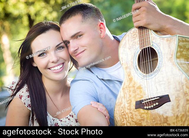 Affectionate mixed-race couple portrait with guitar in the park