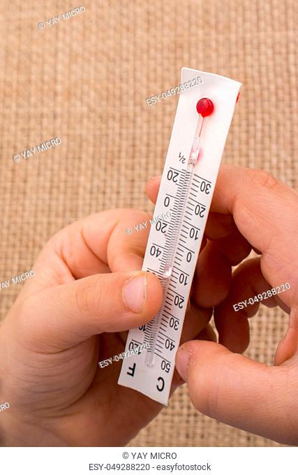 Hand holding a thermometer on a brown color background