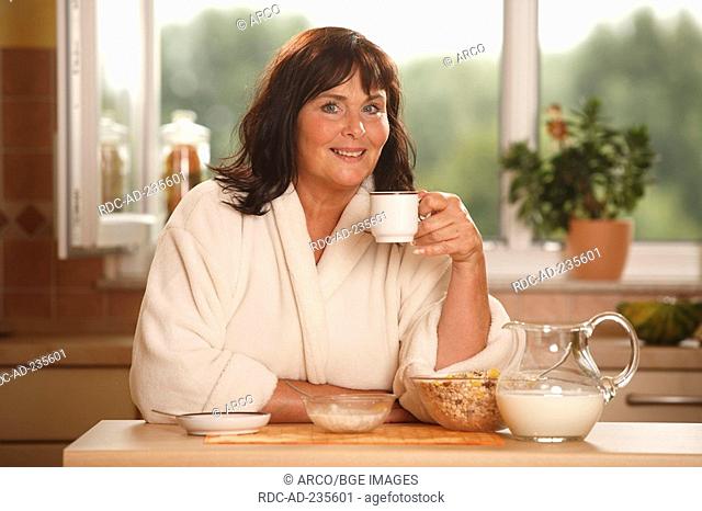 Woman having breakfast / bowl, cup of coffee, pot of milk, muesli