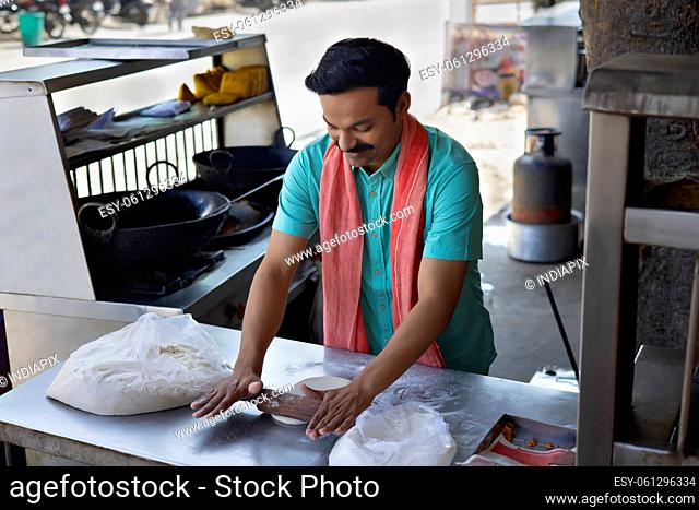 Street food vendor flattening flour dough by rolling pin