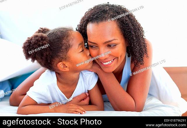 Cute little girl woman kissing her mother lying down on bed
