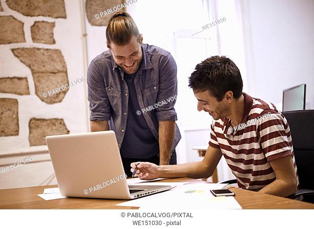 Two handsome young business men planning a presentation for a meeting enjoying a moment of a good idea with toothy smiles