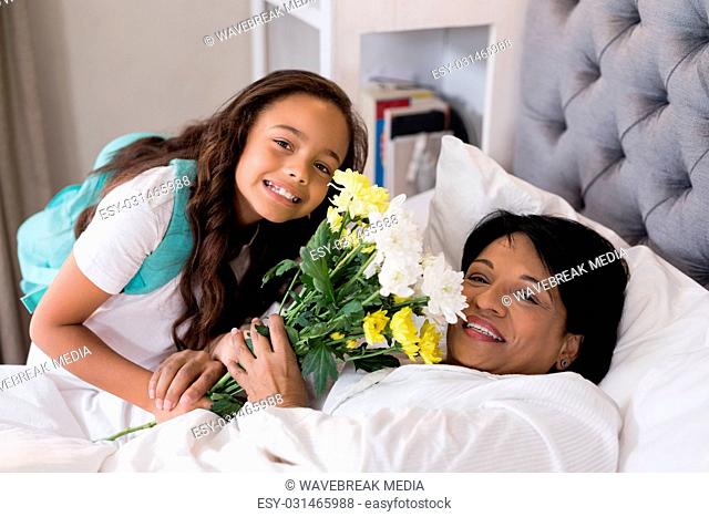 Portrait of smiling grandmother and granddaughter with flower bouquet on bed at home