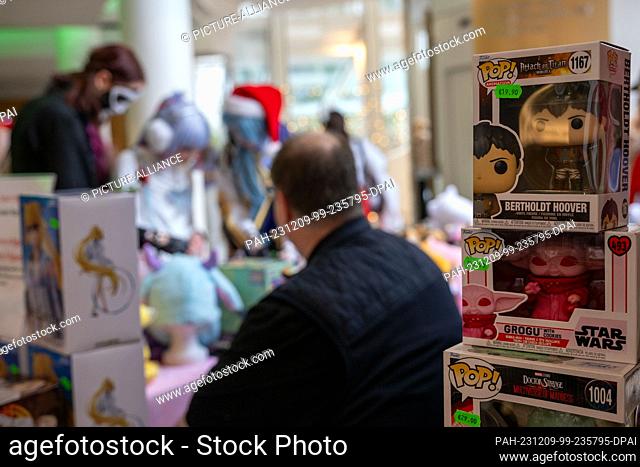09 December 2023, Bavaria, Coburg: Three young women in costumes look at manga merchandise at a stand. The German Xmas Con, a trade fair for anime