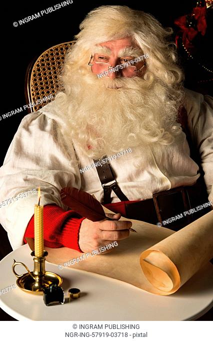Santa Claus sitting at home and writing on old paper roll to do list with quill pen and ink at night with candle light. Authentic vintage style portrait