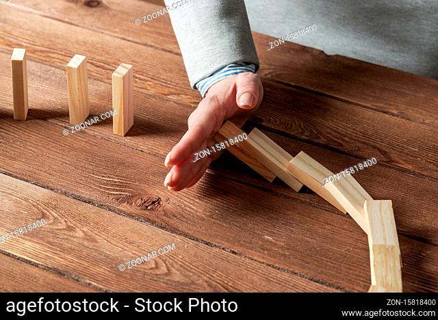 Close up female hand interrupting domino effect. Operative business solution, strategy and successful intervention. Business assistance concept with wooden...