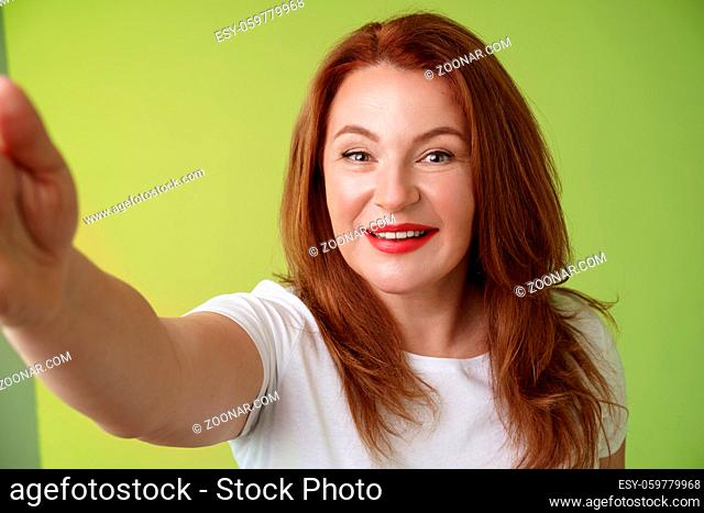 Close-up joyful enthusiastic redhead alluring middle-aged woman extand arm towards camera taking selfie smartphone smiling broadly posing photograph taking...