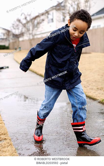 Mixed race boy splashing in rainboots