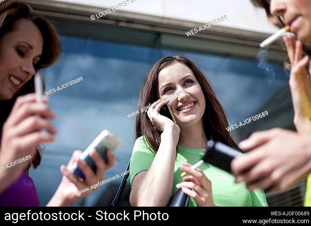 Smiling businesswoman talking on phone while smoking cigarette with colleagues