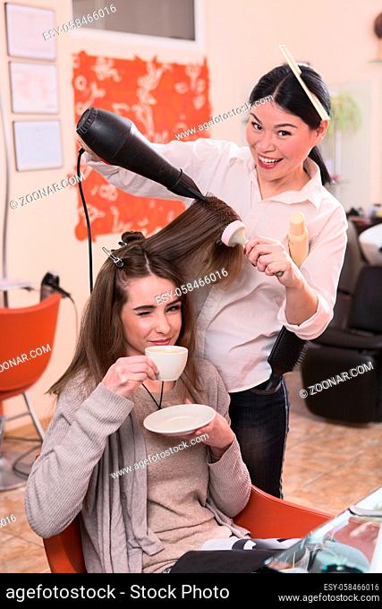 Young woman looking at camera together with hairdresser. Beautiful lady drinking coffee while having her hair washed in hairdressing saloon