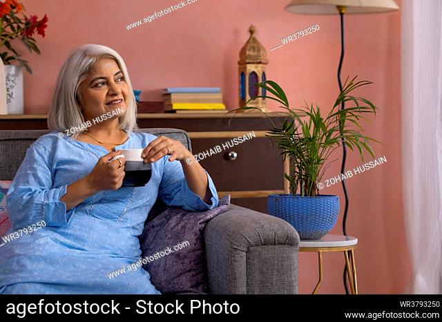 Old woman with holding a cup of tea in hand looking away and thinking