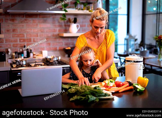 Caucasian woman and her daughter spending time in the kitchen and using a laptop
