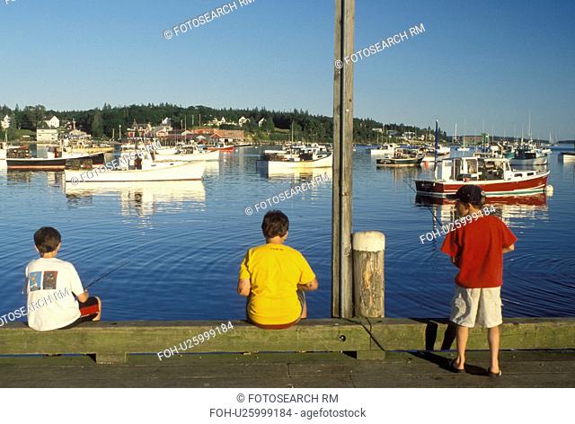 fishing, Bass Harbor, Mount Desert Island, ME, Maine, Boys fishing off the pier with view of lobster fishing boats buoyed in the harbor in the fishing village...