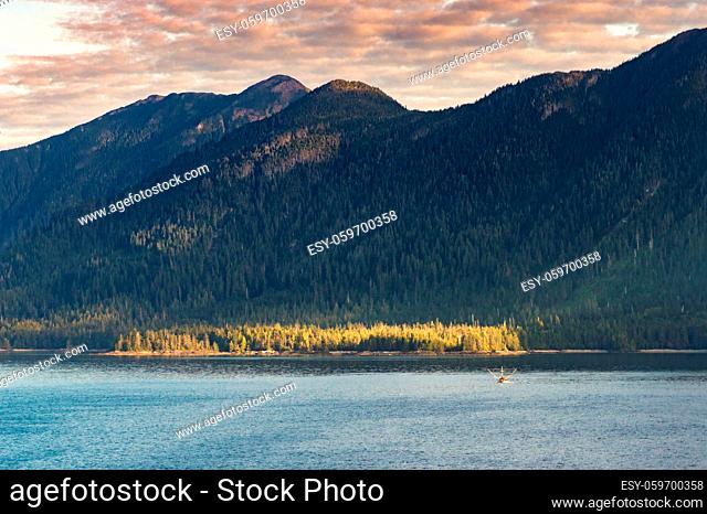 Small fishing troller in distance below mountains, early morning in Clarence Strait near Ketchikan, Alaska