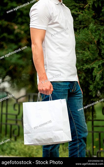 man with a white paper bag in hands on a park background. courier with a bag on the background of a green park