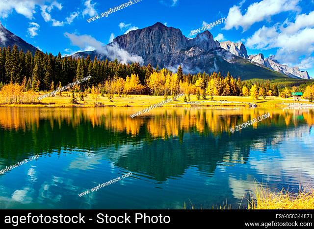 The Canadian Rockies. The city of Canmore in Banff Park. Bright autumn forest is reflected in the smooth water of the lake