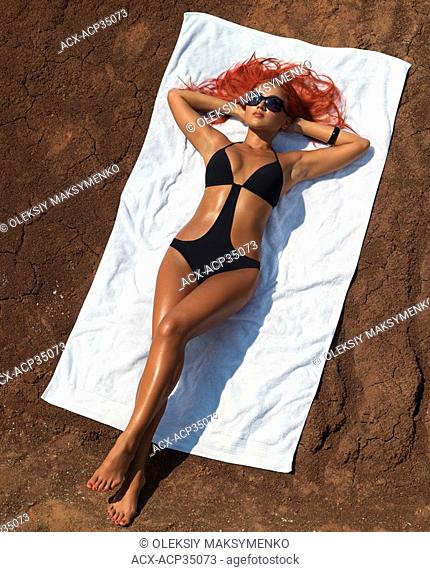 Beautiful suntanned woman lying on a beach towel on dry red soil