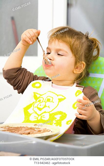Toddler girl is eating with spoon