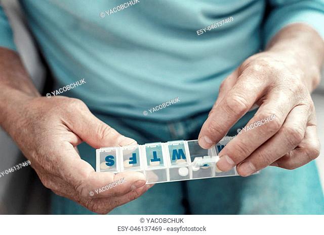 One more pill. Senior ill aging man keeping pack of medicine sitting and taking pill