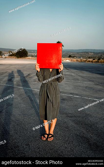 Woman covering face with red placard while standing at road
