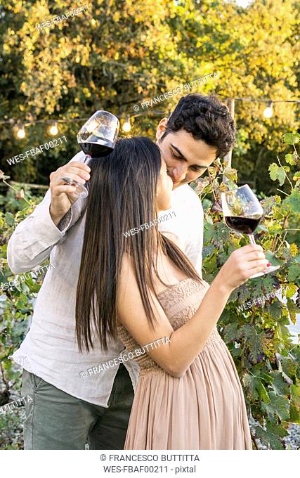 Italy, Tuscany, Siena, affectionate young couple with red wine glasses in a vineyard