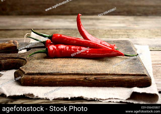 red chili peppers on a brown cutting wooden board, gray table, close up