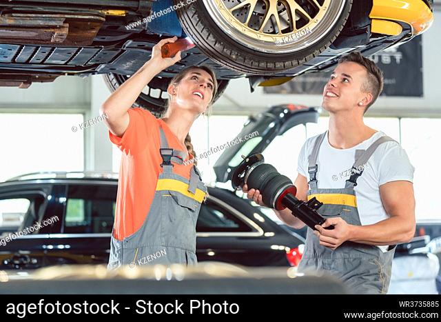 Experienced female auto mechanic checking tires before installing together with her colleague a new air suspension system in a modern automobile repair shop