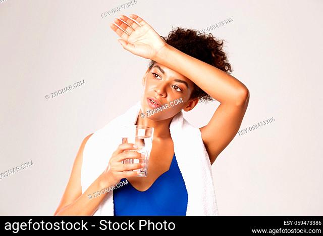 Close-up of tired african-american fitness woman, drinking water and wiping sweat off forehead after workout training session, holding towel on shoulders