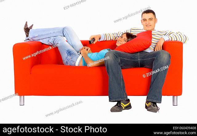 Man and woman sitting on a red couch with remote control. Isolated on white background, in studio