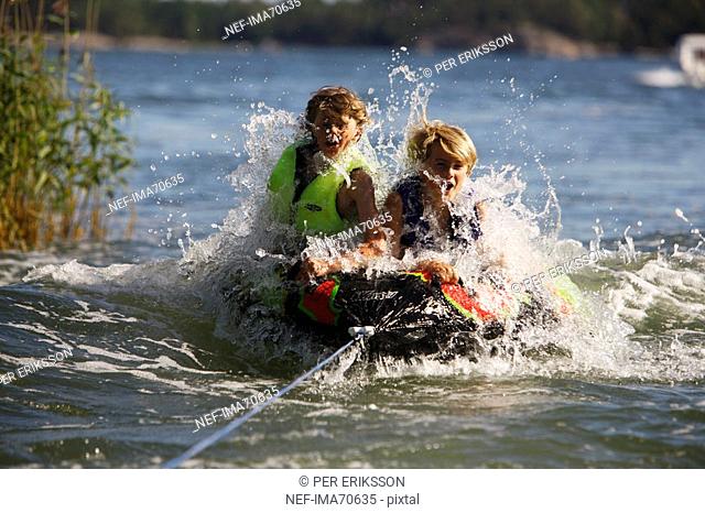 Boys riding on a plastic object drawn by a motorboat, Sweden
