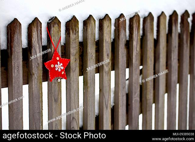 winterly Christmas scenery with red white felt star ornament hanging from snow covered wooden fence